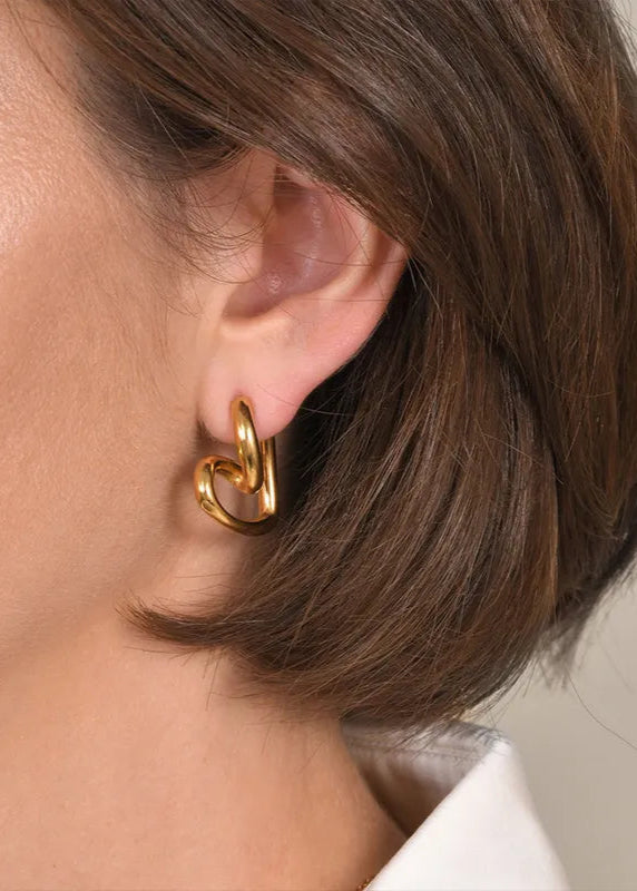 A close-up image of a person wearing gold-colored heart-shaped hoop earrings.