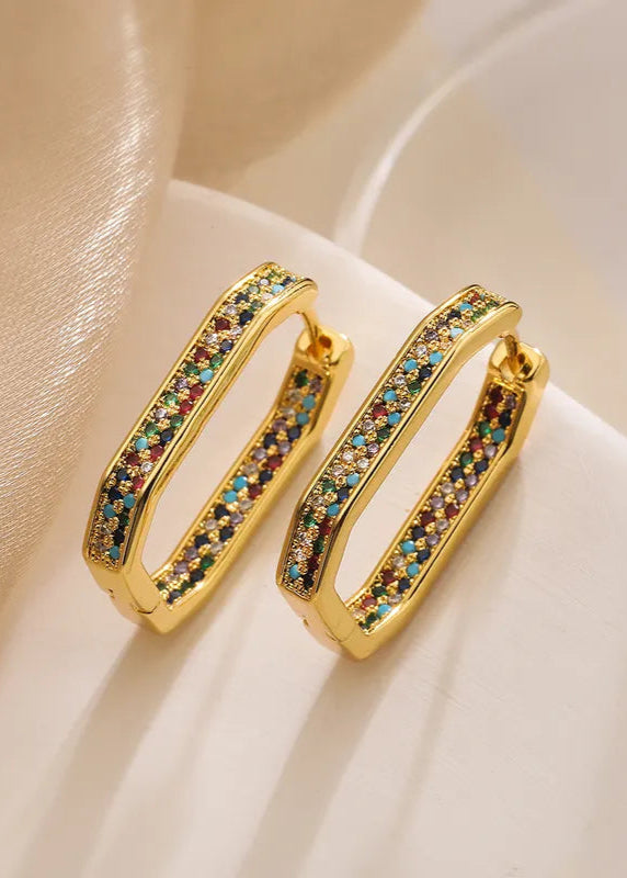 A pair of hexagonal-shaped hoop earrings with gold plating and multicolored pave stones on a white fabric surface.