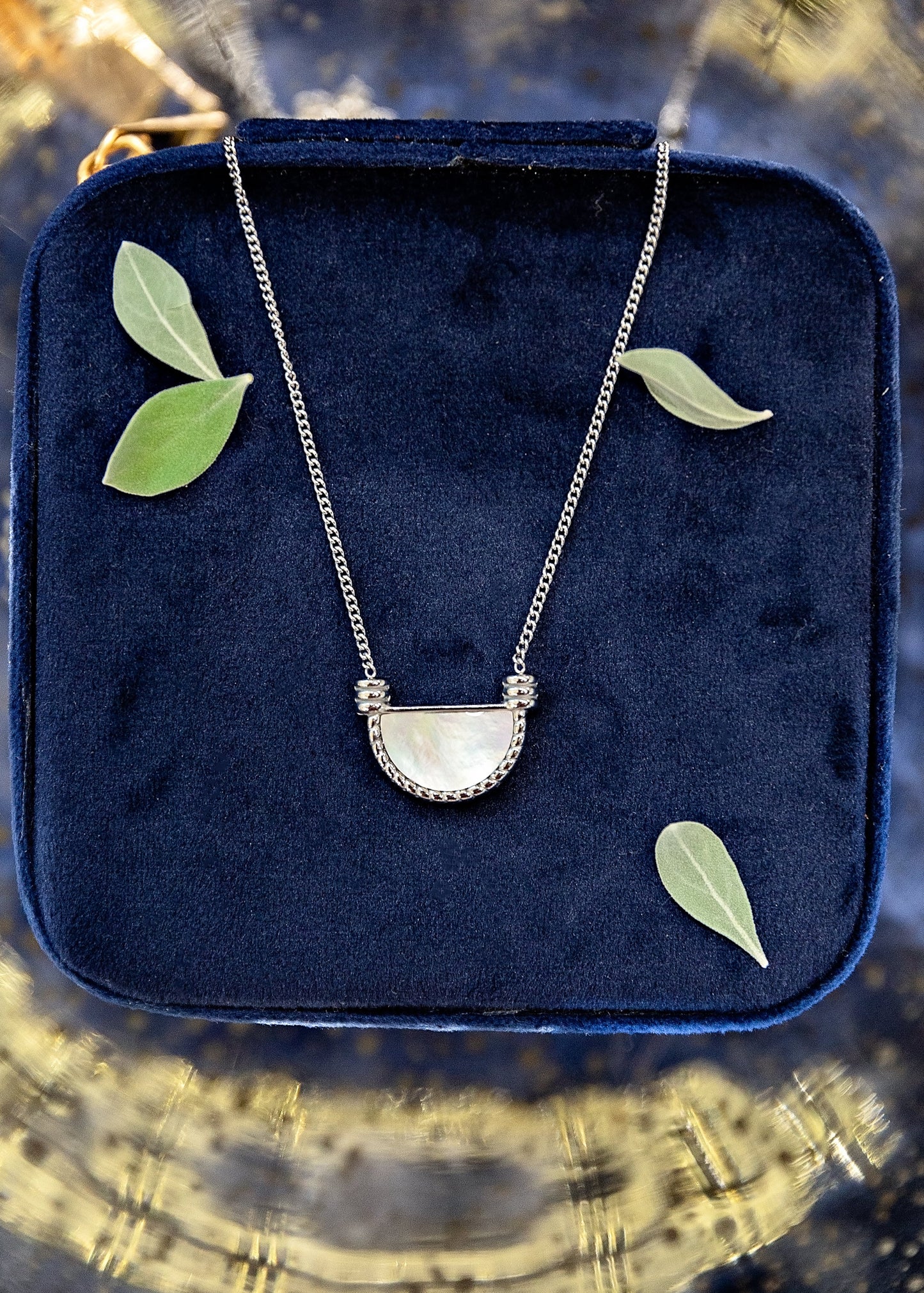 Necklace with a half-moon pendant on a blue velvet cushion with leaves