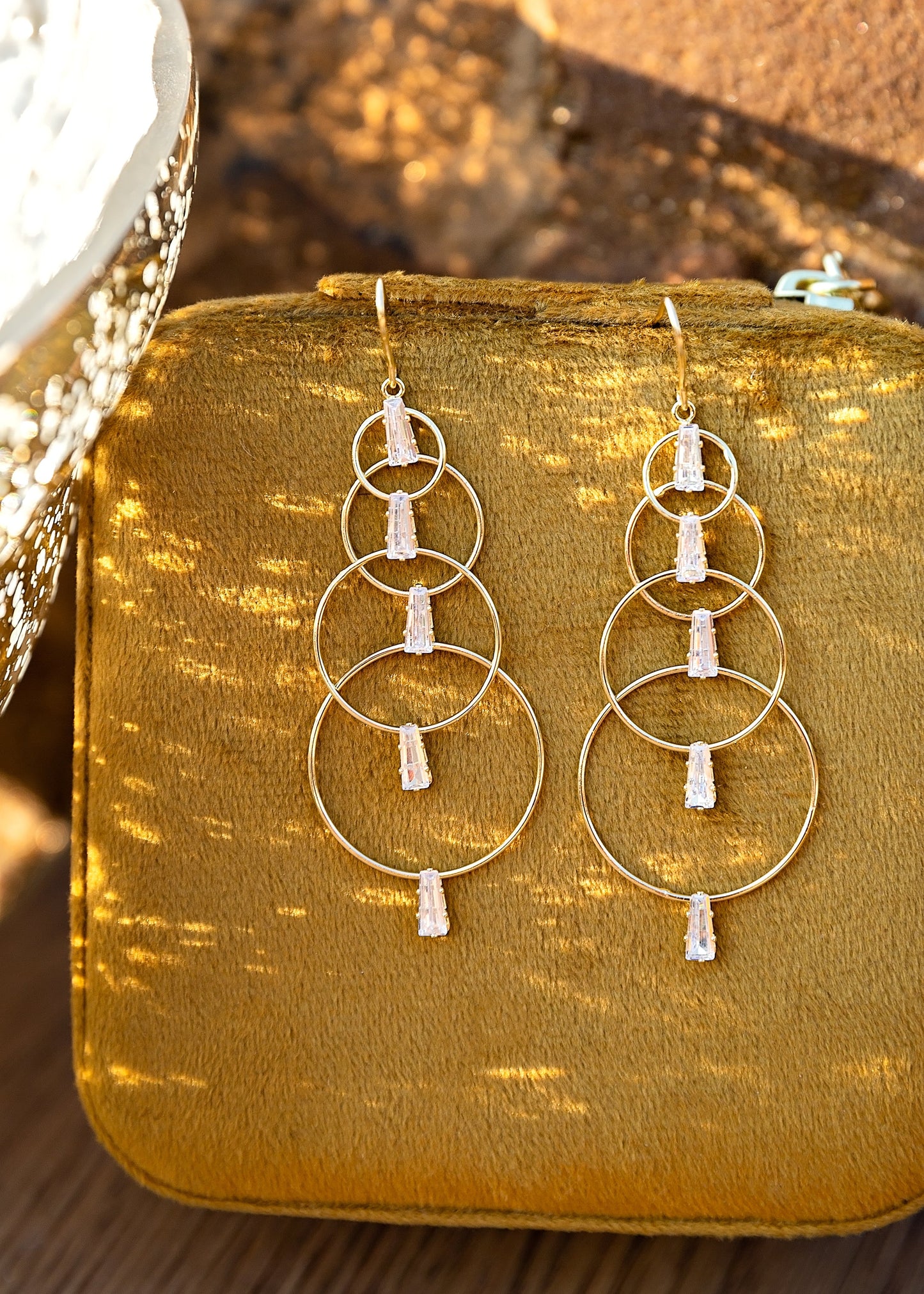Gold hoop earrings with white stones on a mustard yellow fabric background