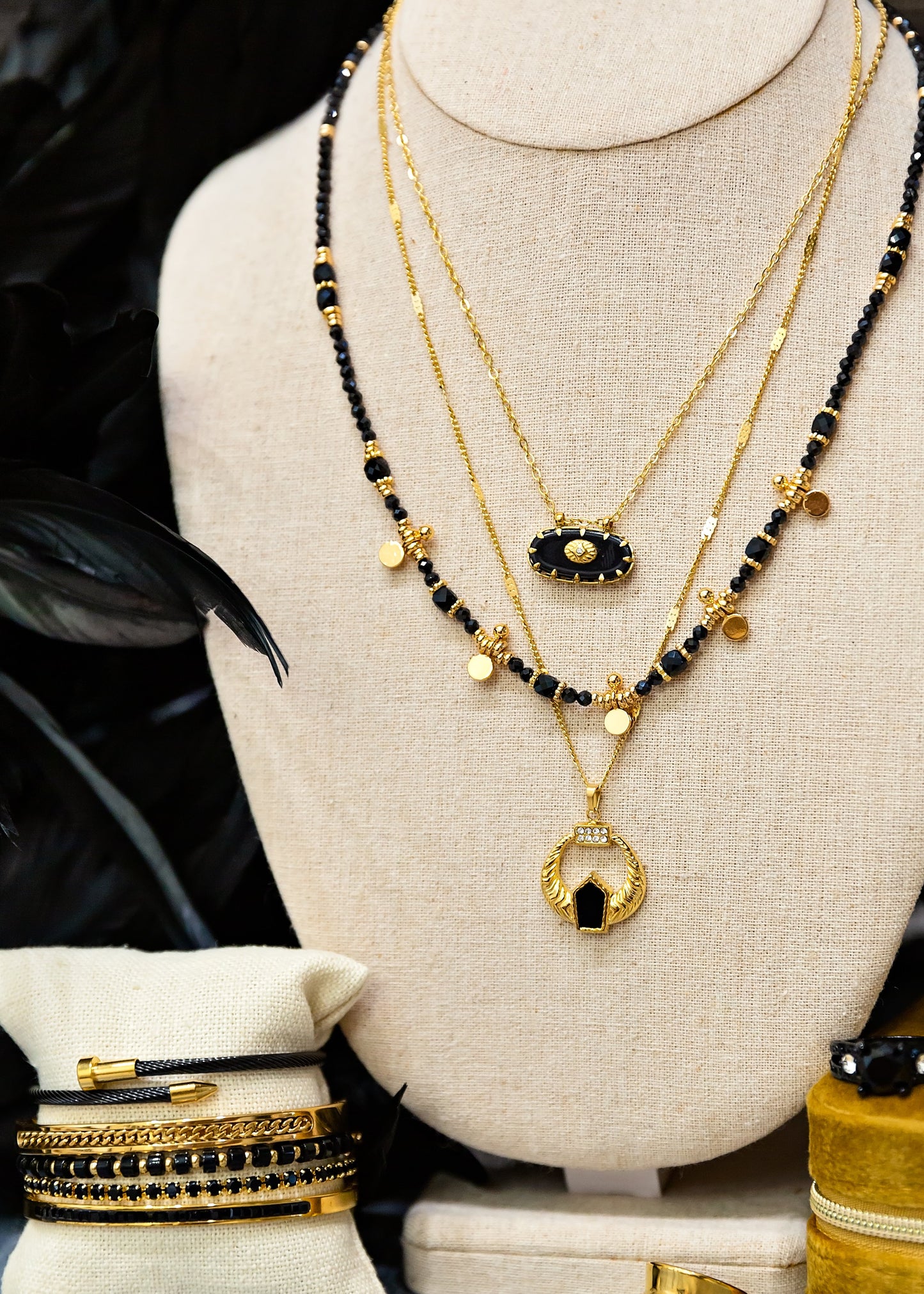 Mannequin wearing gold and black necklaces with bracelets and rings on a table.