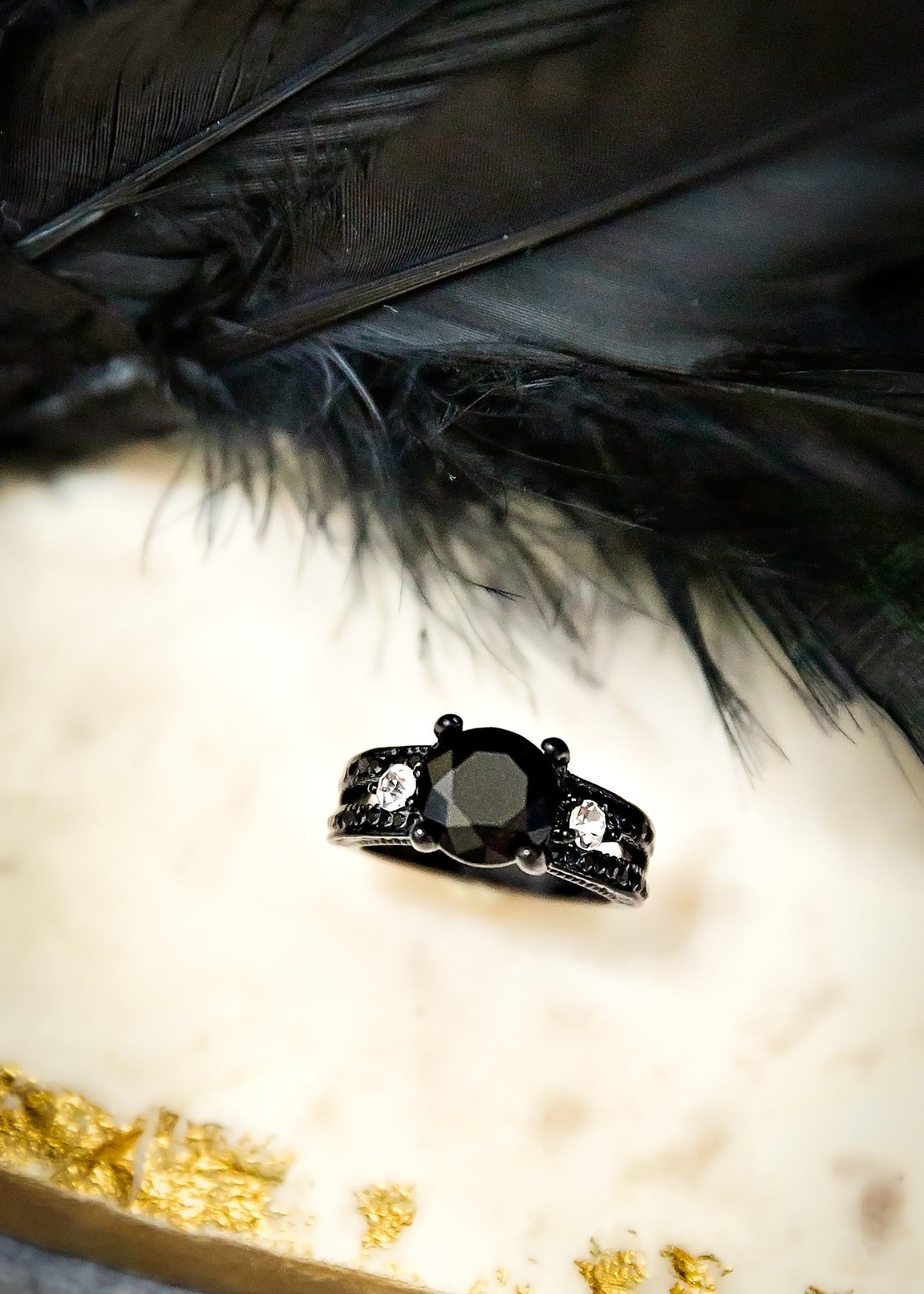 Black ring with gemstone on a white surface with black feathers