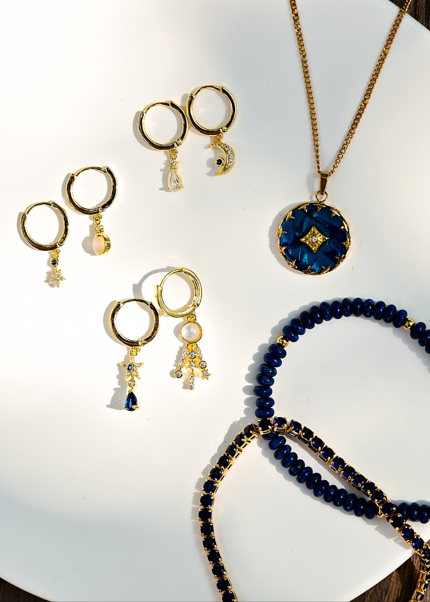 Gold and blue jewelry including earrings and a necklace on a white surface.