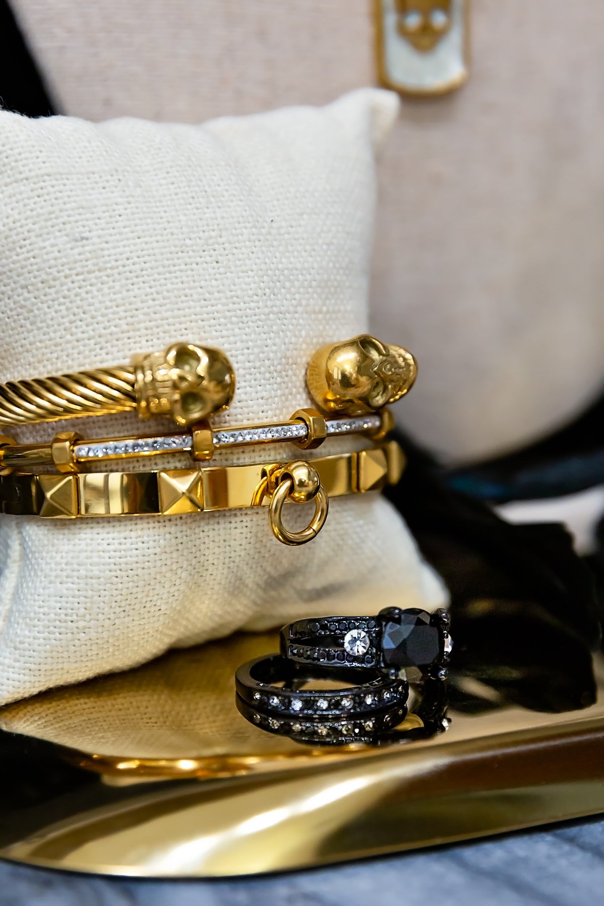 Gold bracelet and black ring on a reflective surface with a neutral background