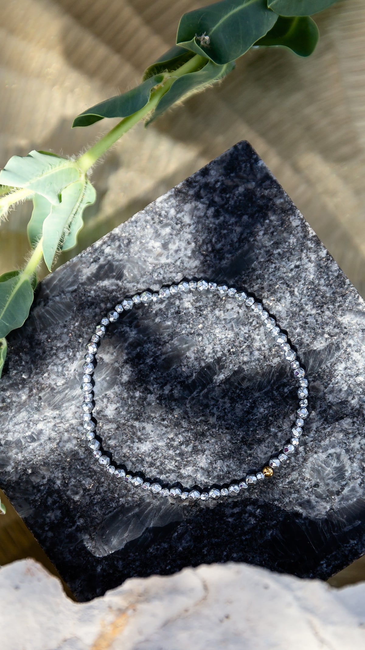 Lumen Bracelet from the LUNA Collection featuring dark faceted beads and an 18kt gold-plated accent bead, styled on natural stone.