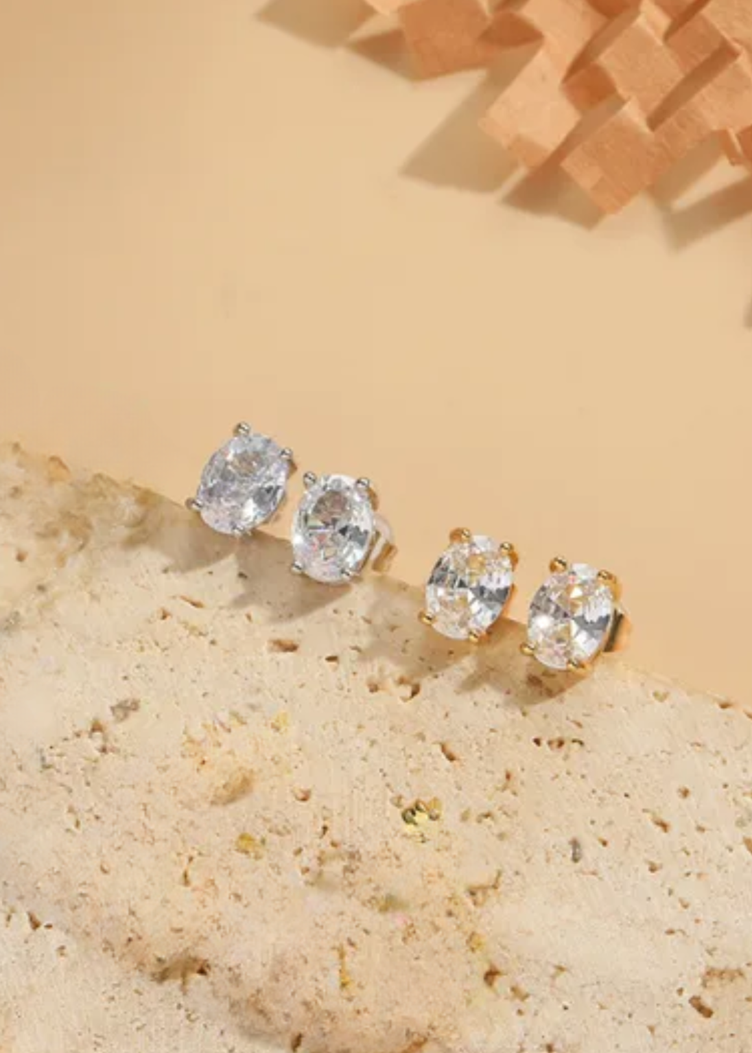 A set of oval cz stones stud earrings in 14kt gold plating, displayed on a textured surface with a neutral background.