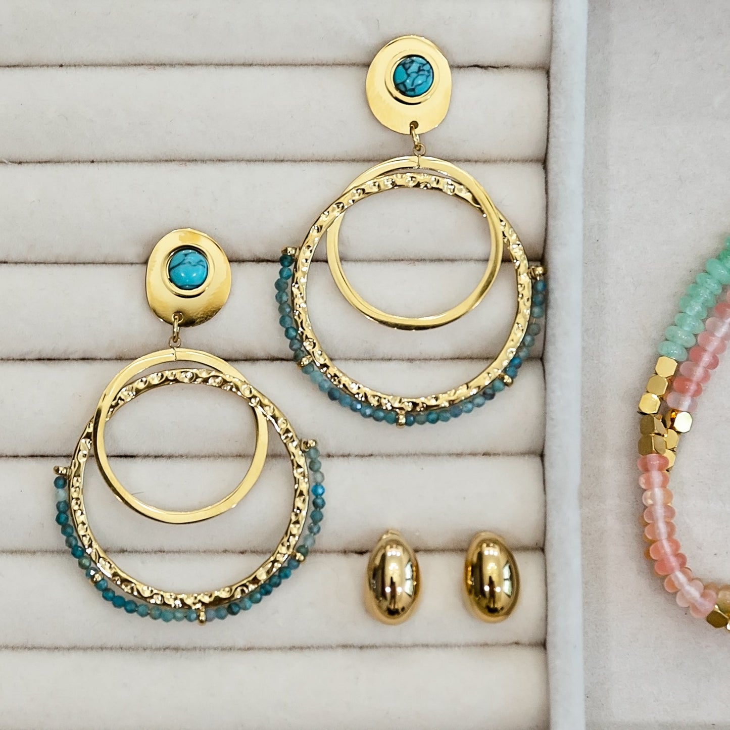 Gold and turquoise hoop earrings on a textured surface