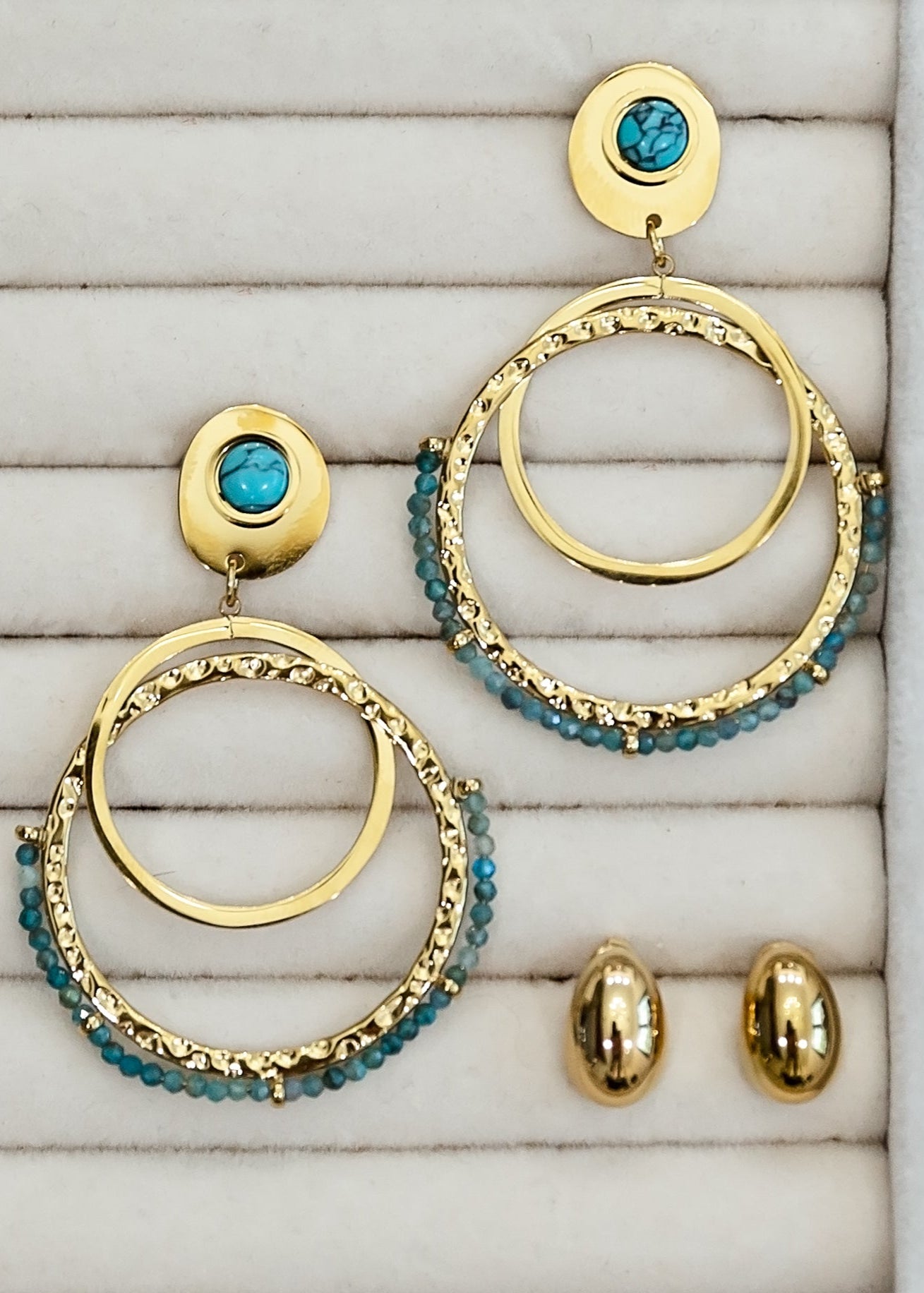Gold and turquoise hoop earrings on a textured surface