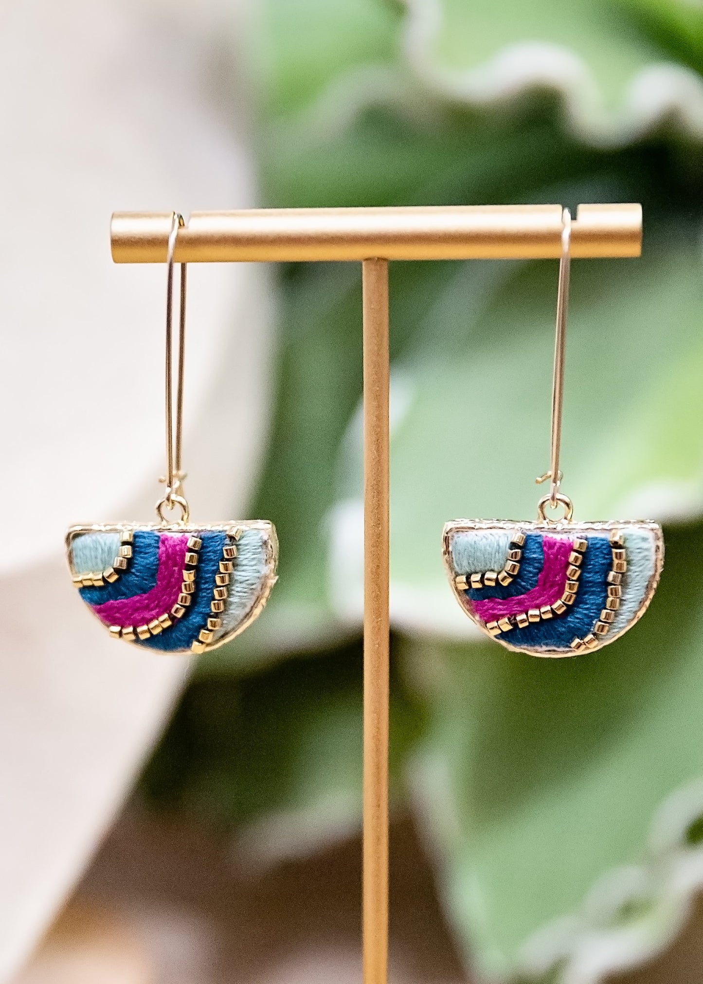 Colorful earrings on a gold earring stand with a green leafy background