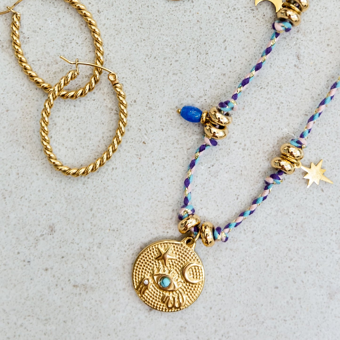 Gold hoop earrings and necklaces with decorative pendants on a textured surface