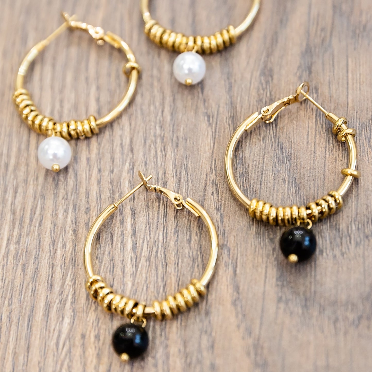 Gold hoop earrings with black and white beads on a wooden surface