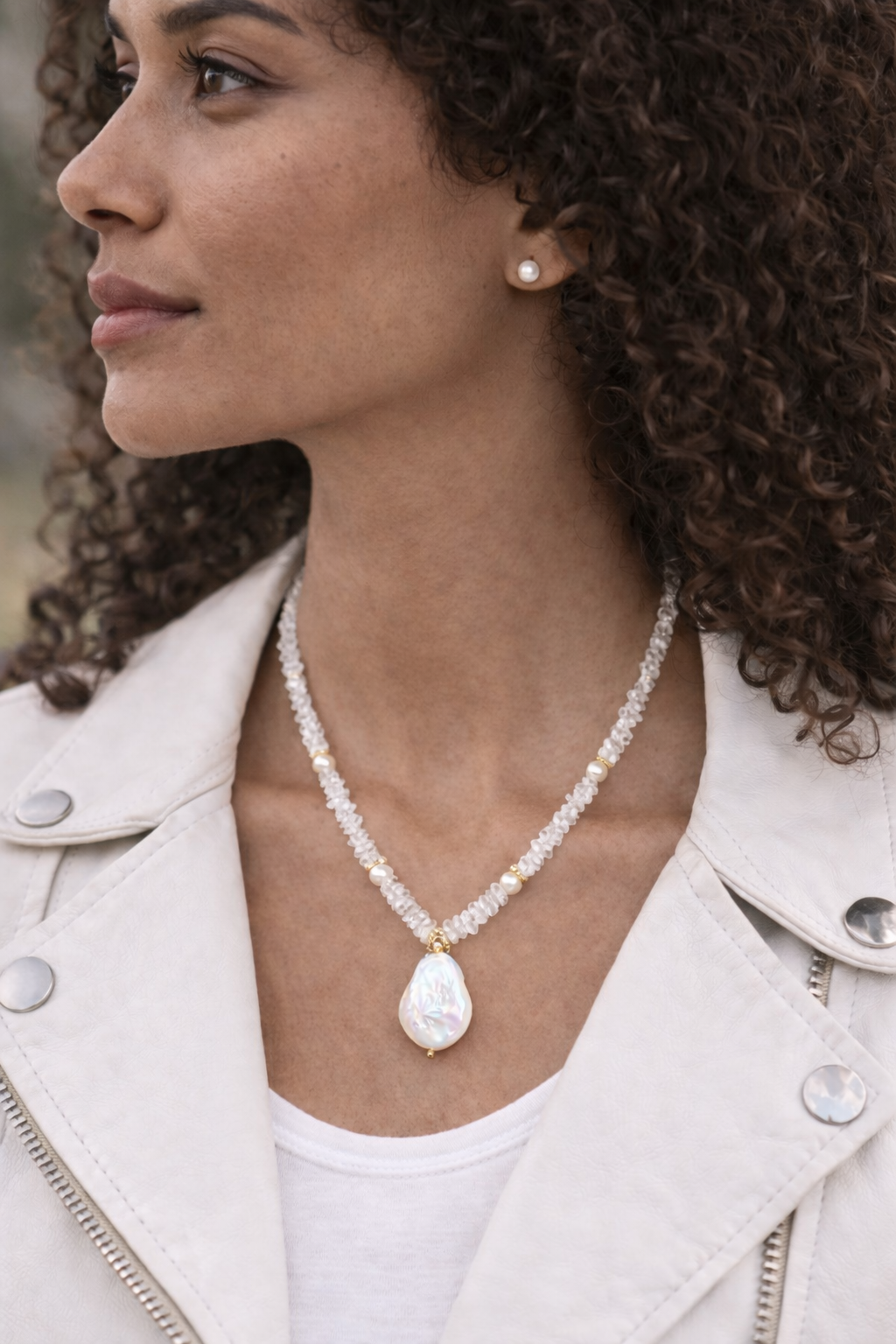 Woman wearing a pearl necklace ande pearl stud earrings with a white leather jacket.