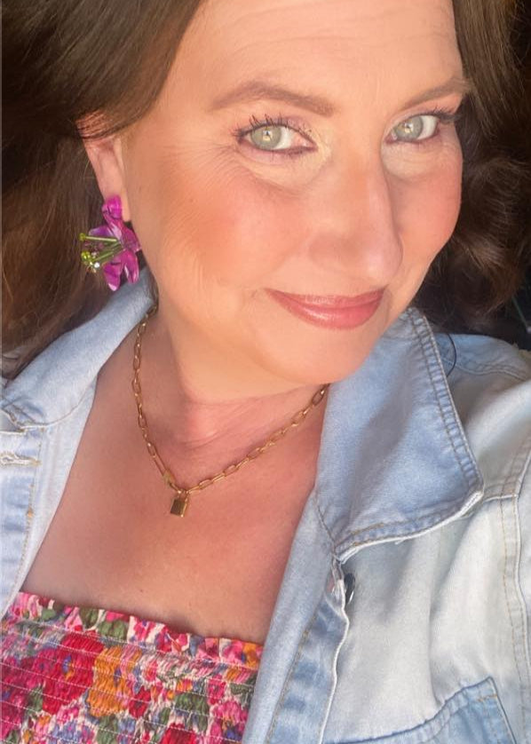 Woman wearing a denim jacket over a floral dress with a colorful earring.