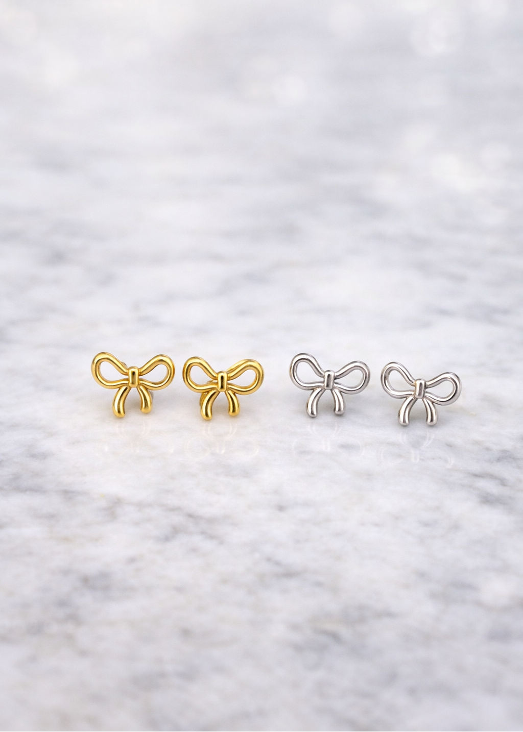 Four bow-shaped earrings in gold and silver on a textured white background