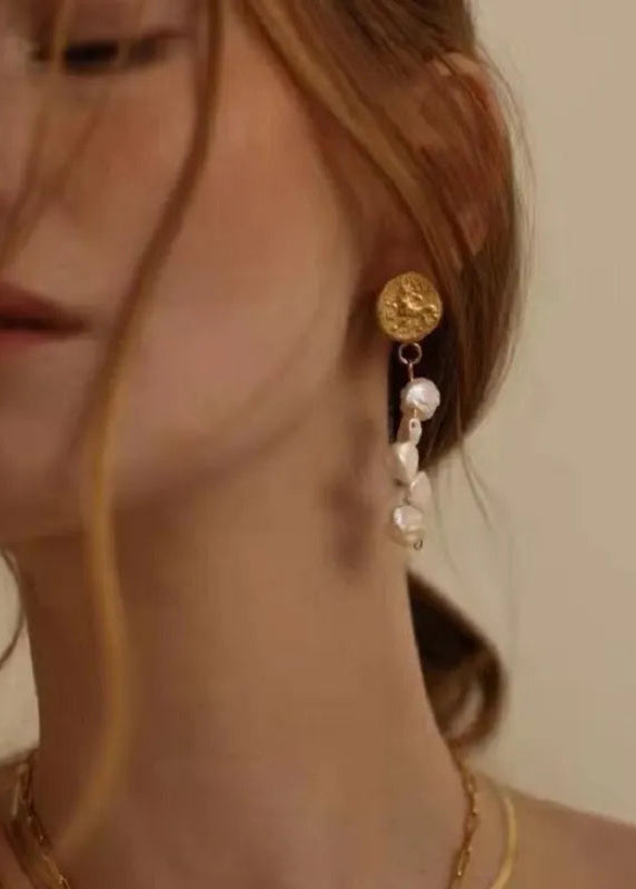 A person wearing a gold-plated earring with a large baroque pearl drop.