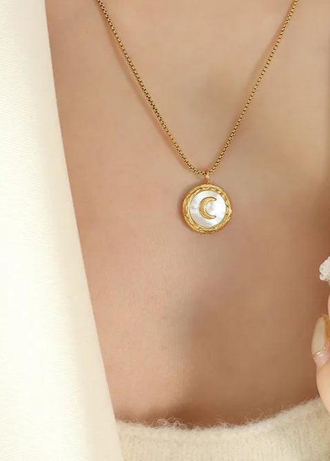Gold necklace with a moon pendant worn by a person, against a neutral background