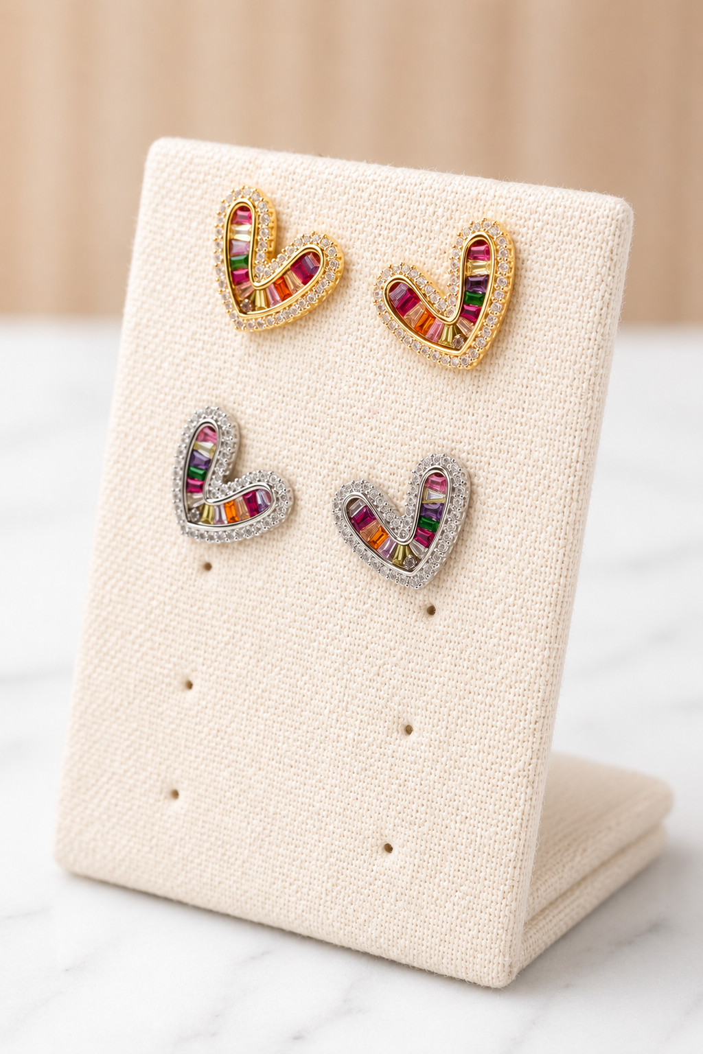 Simone Heart Studs in gold and silver with multicolor baguette gemstones on an angled linen earring display stand