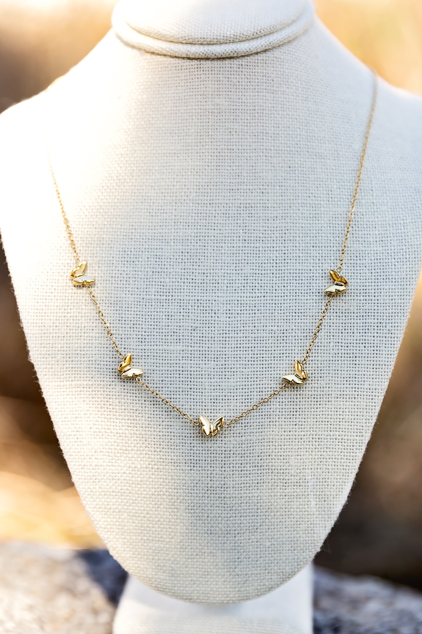 Gold butterfly charm necklace with delicate chain displayed on jewelry bust
