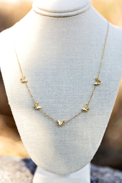 Gold butterfly charm necklace with delicate chain displayed on jewelry bust