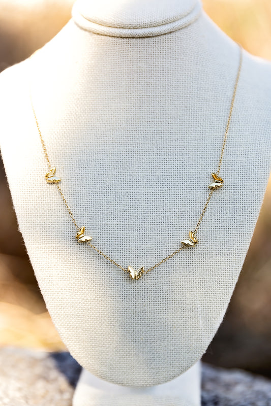 Gold butterfly charm necklace with delicate chain displayed on jewelry bust