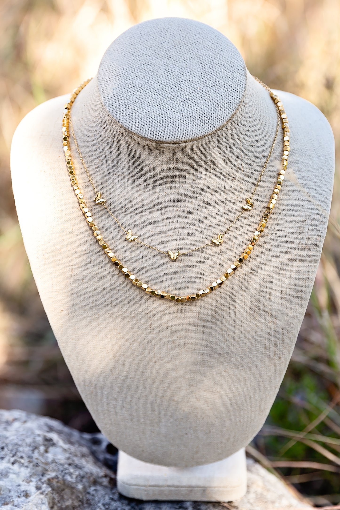 Gold butterfly necklace layered with other chains on jewelry bust for styling inspiration