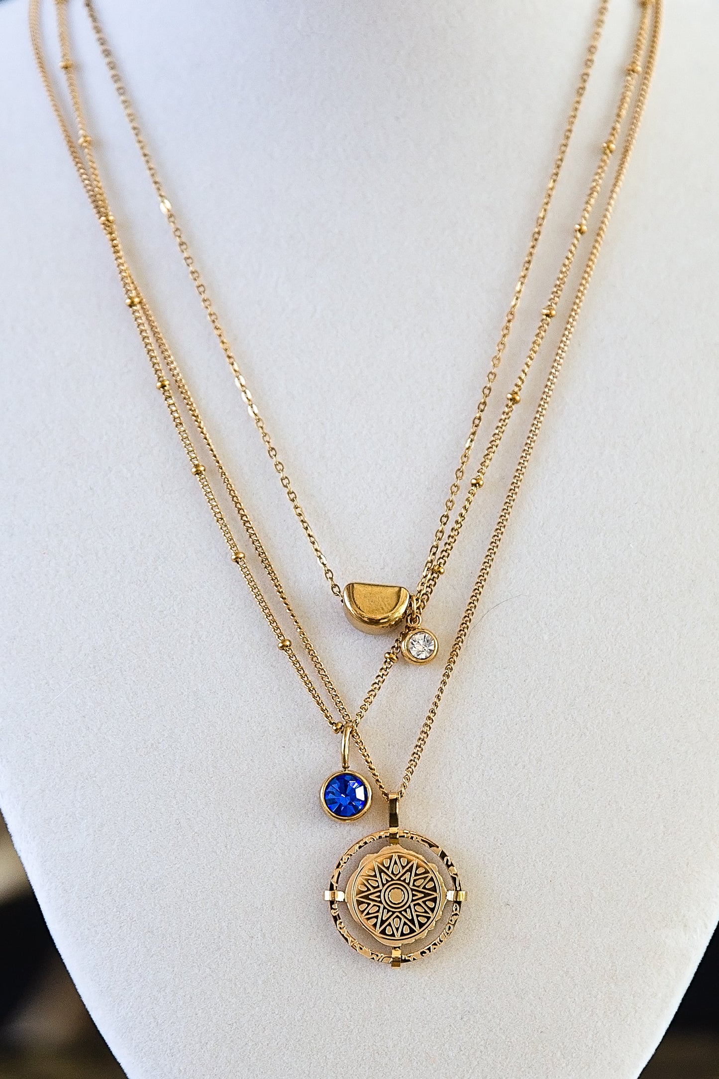 Gold compass pendant necklace layered with other chains on a jewelry display bust