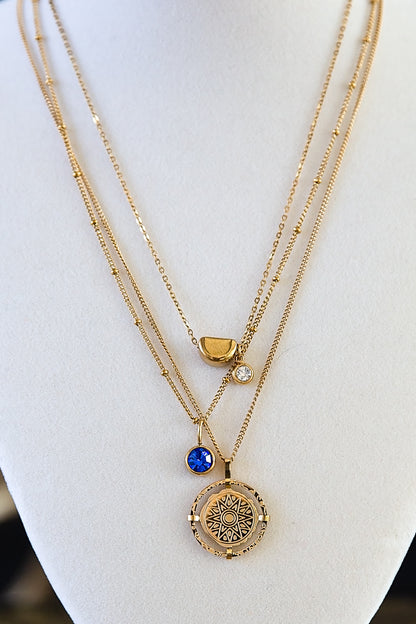 Gold compass pendant necklace layered with other chains on a jewelry display bust