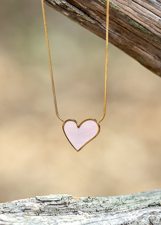 Heart-shaped pendant necklace on a wooden surface with a blurred natural background