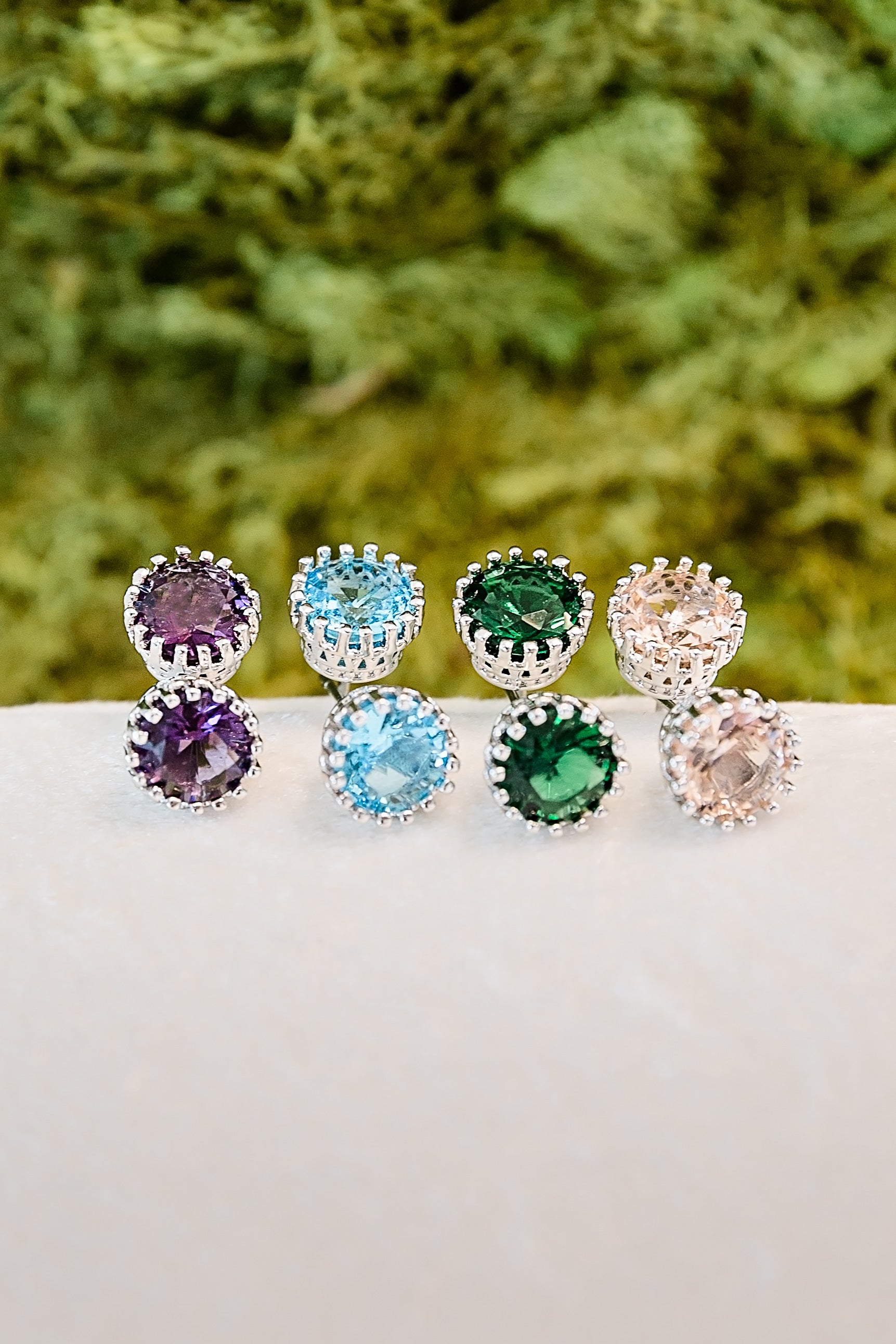 Multiple zircon stud earrings in different colors arranged on natural moss background