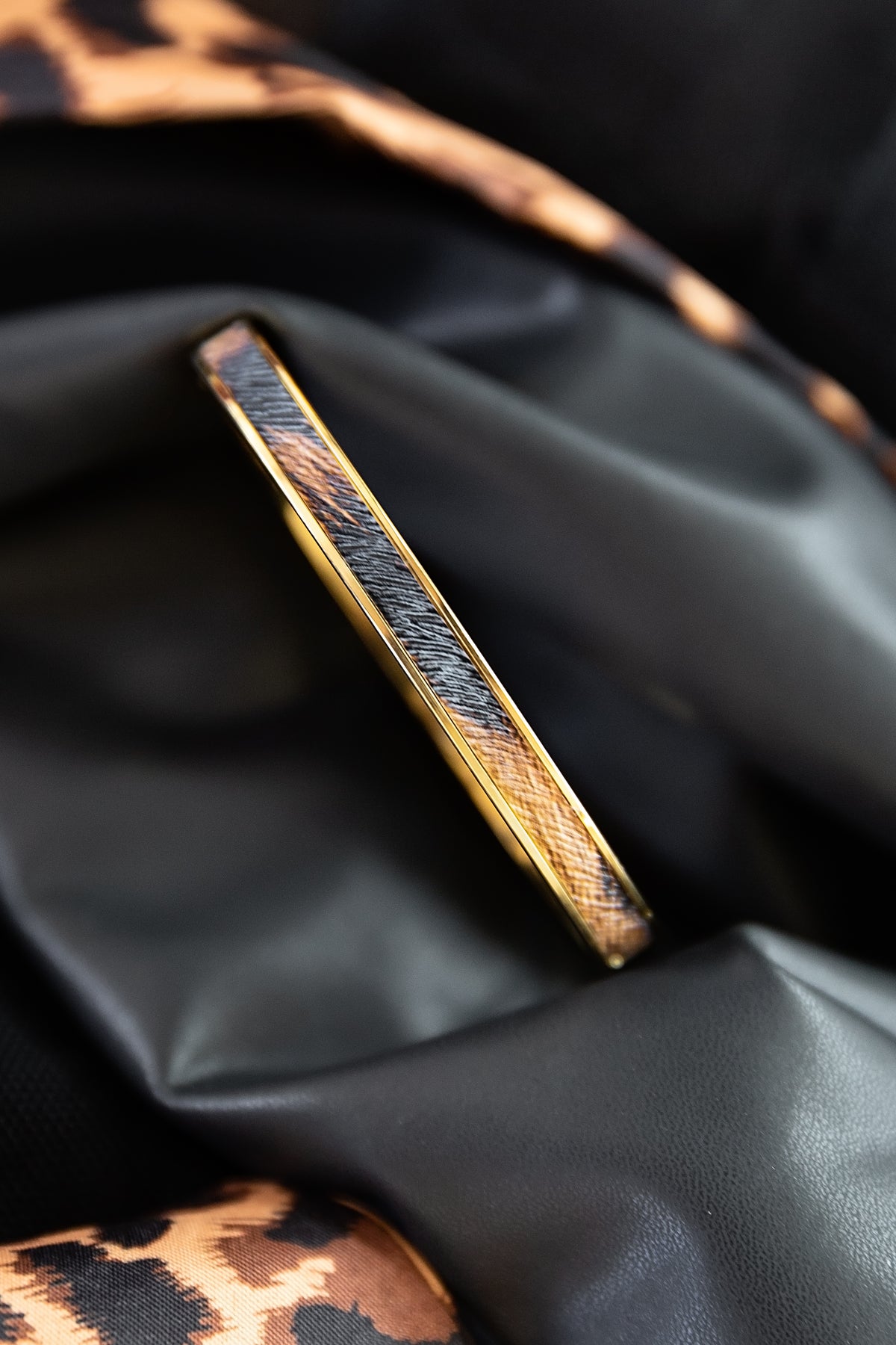 Cheetah Bangle featuring a slim gold design with cheetah-inspired detailing displayed on black fabric.
