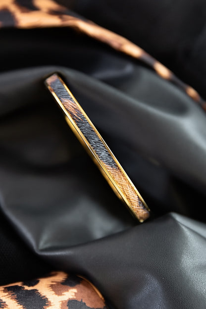 Cheetah Bangle featuring a slim gold design with cheetah-inspired detailing displayed on black fabric.
