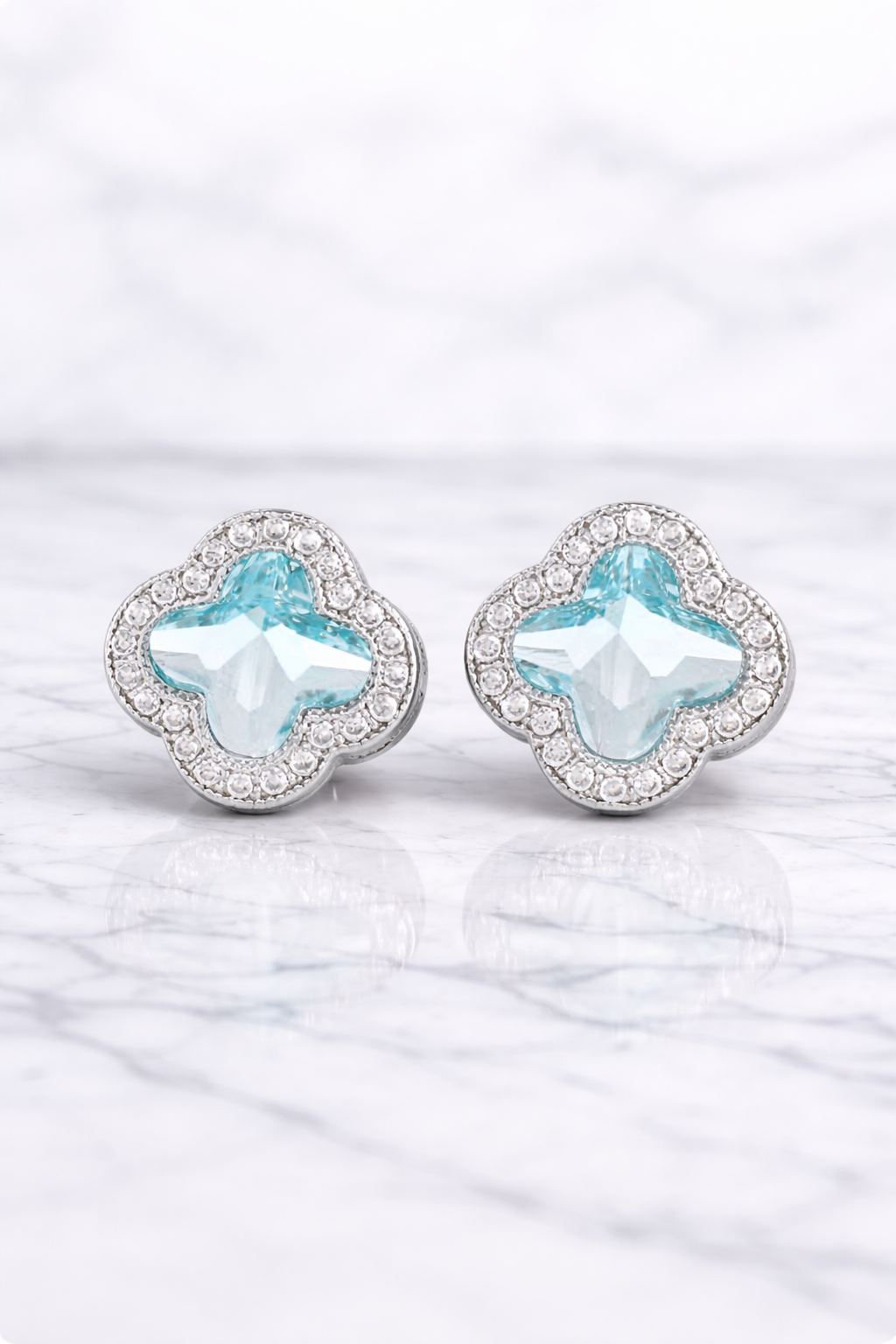Pair of earrings with light blue clover-shaped stones on a white background