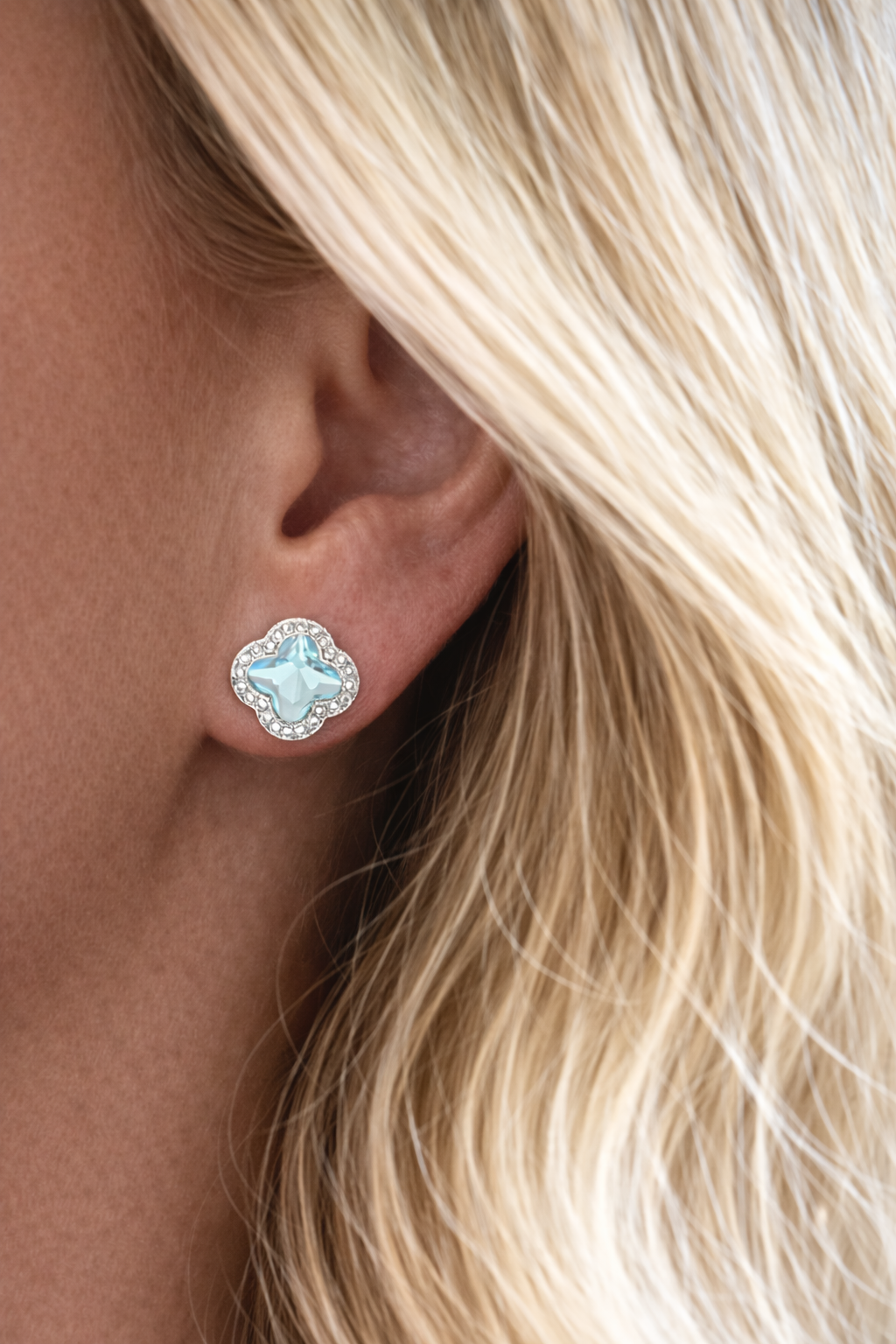 Close-up of a person wearing a silver earring with a clear gemstone.