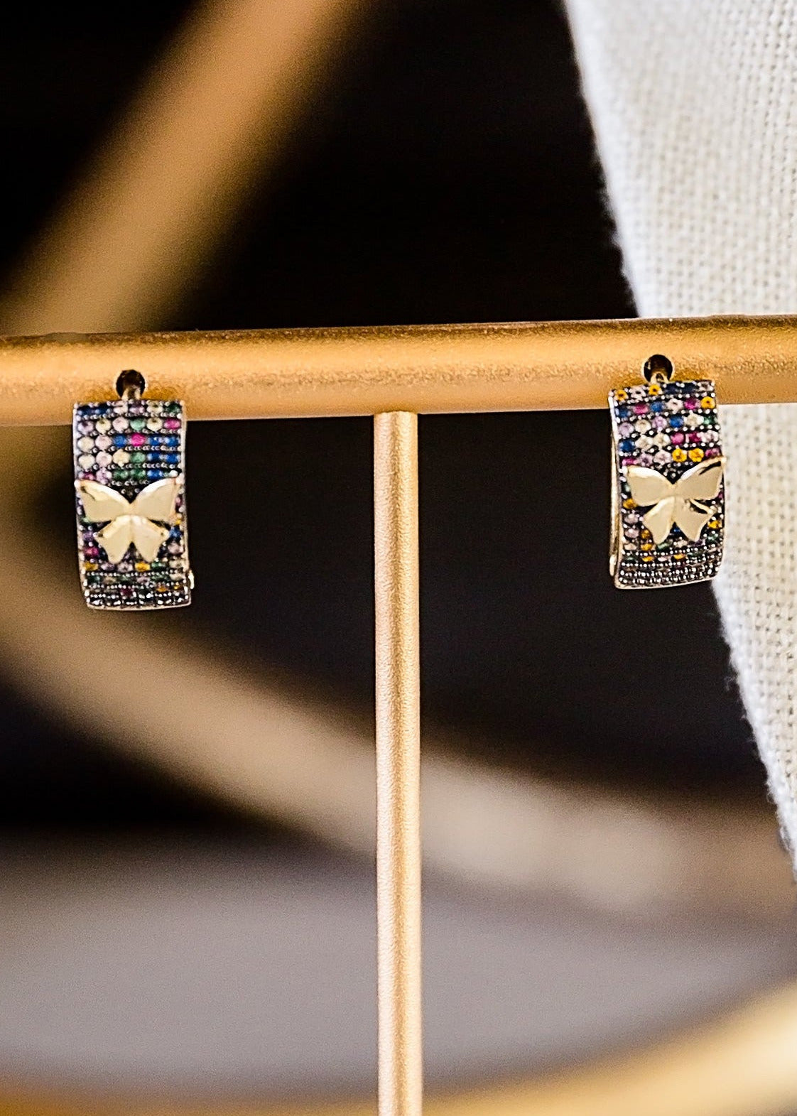 Closeup Mora butterfly earrings with multicolored zircon stones displayed on gold stand, featuring 14kt gold plated brass design