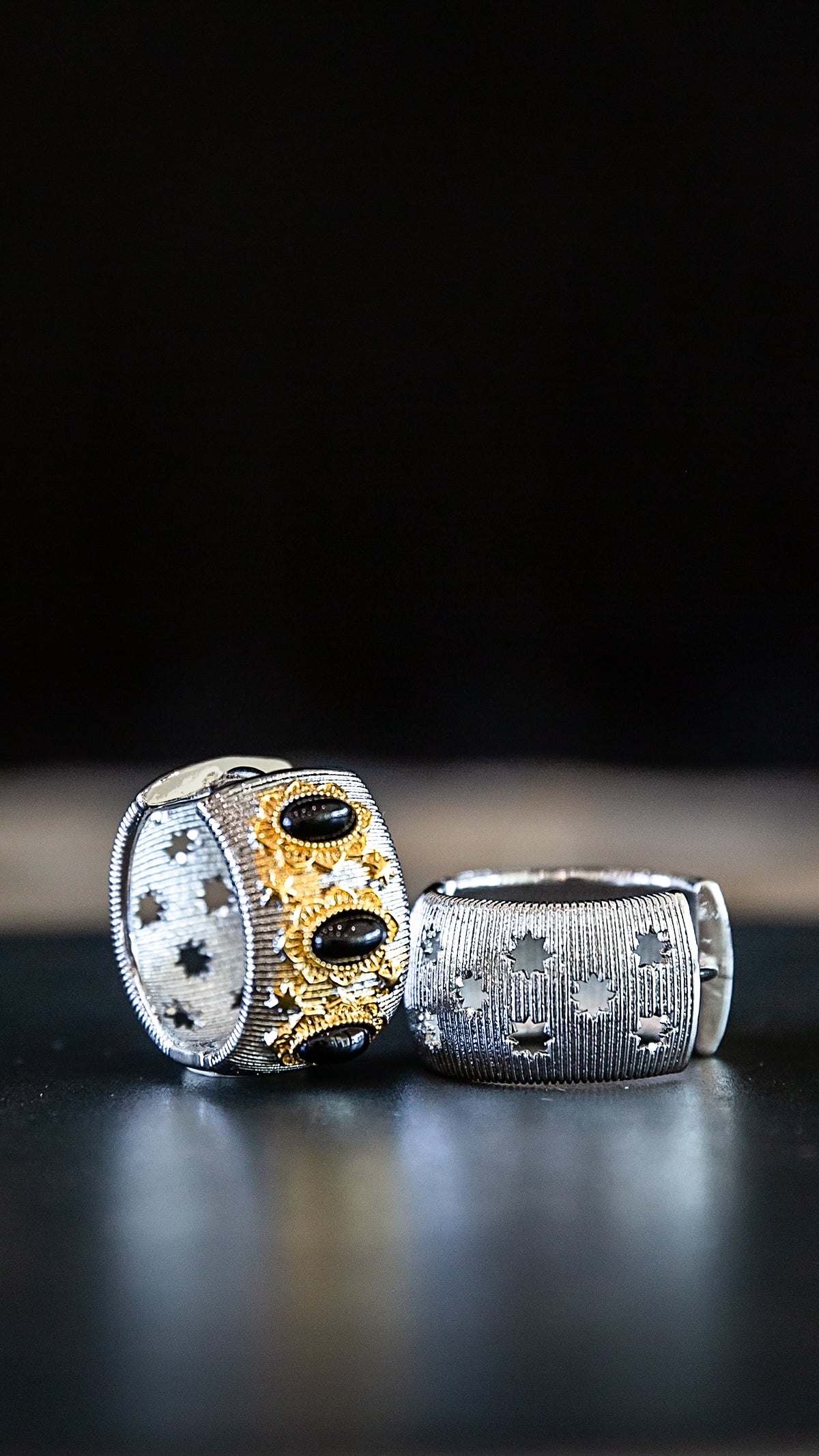 Eclipse Hoops featuring a sculptural silver-tone design with gold and dark accents displayed on a black surface.