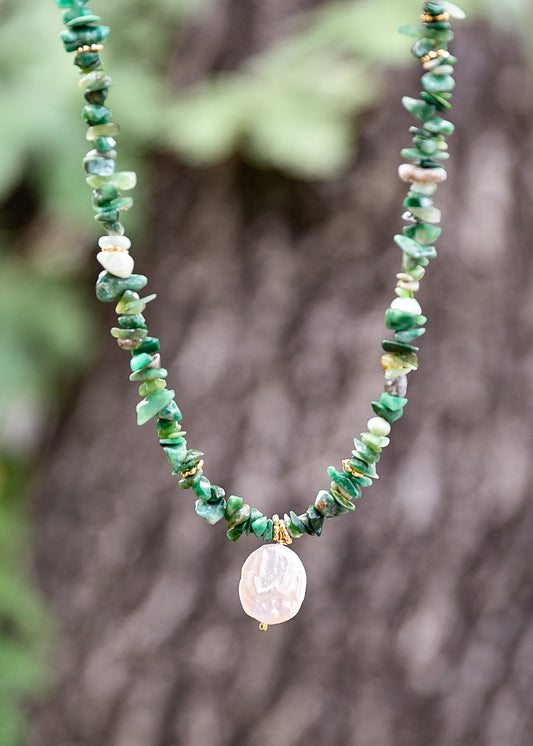 Necklace with green beads and a central pendant against a blurred natural background