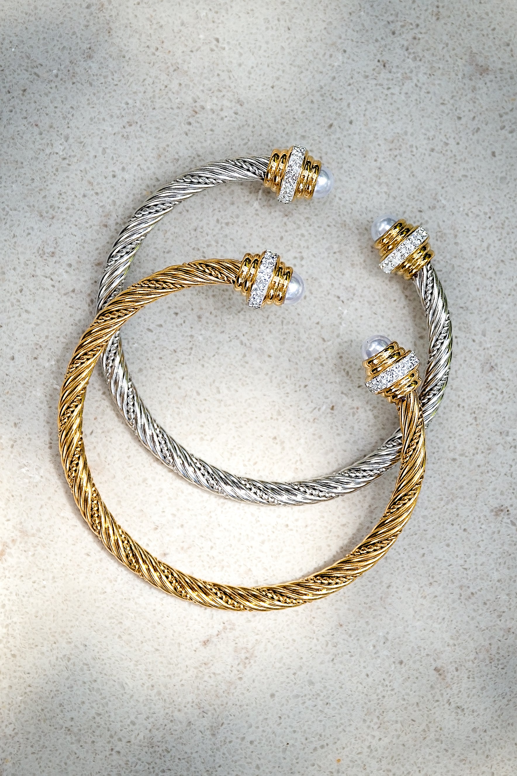 Two gold and silver bracelets on a textured surface