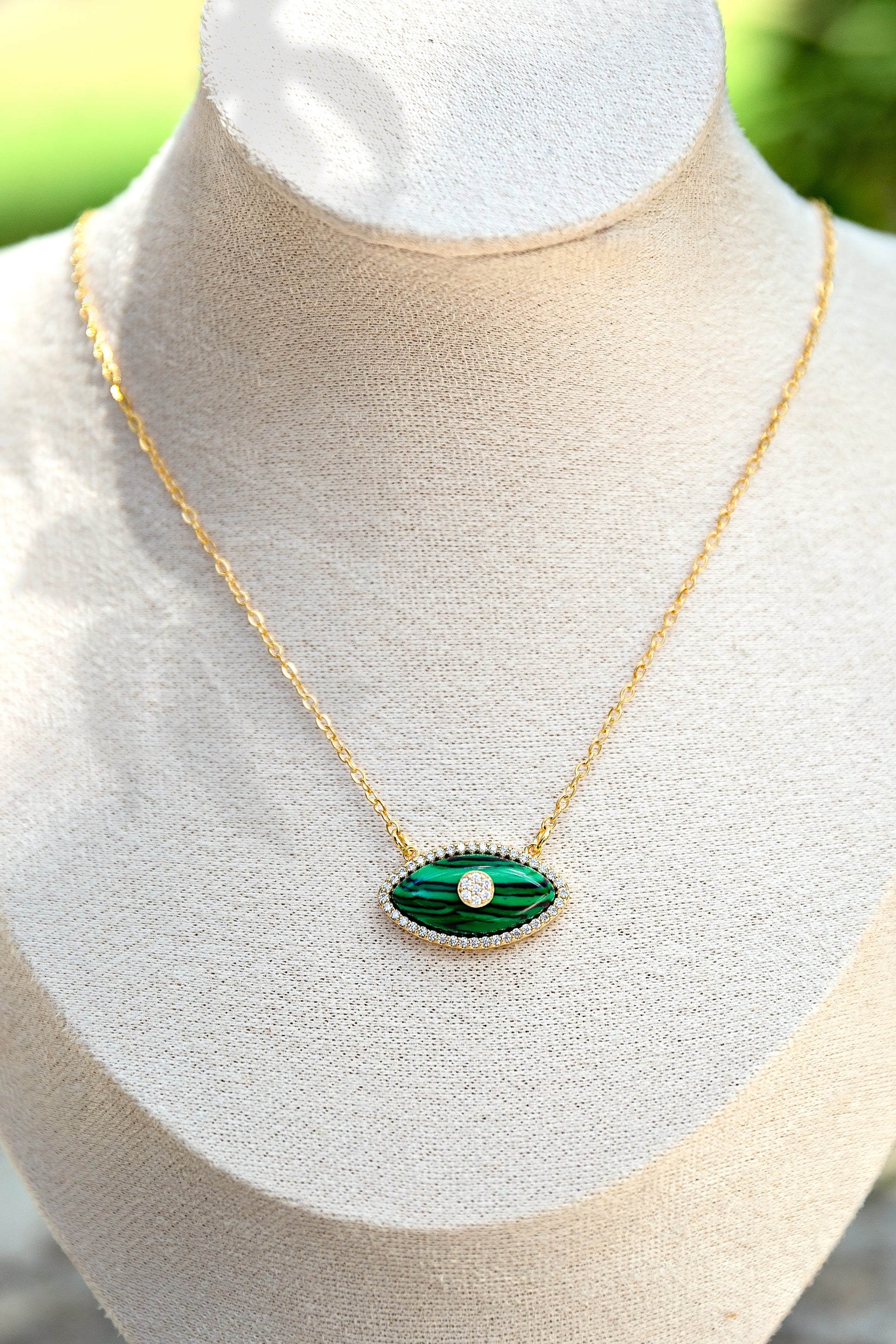 Gold necklace with a green eye-shaped pendant on a mannequin bust.