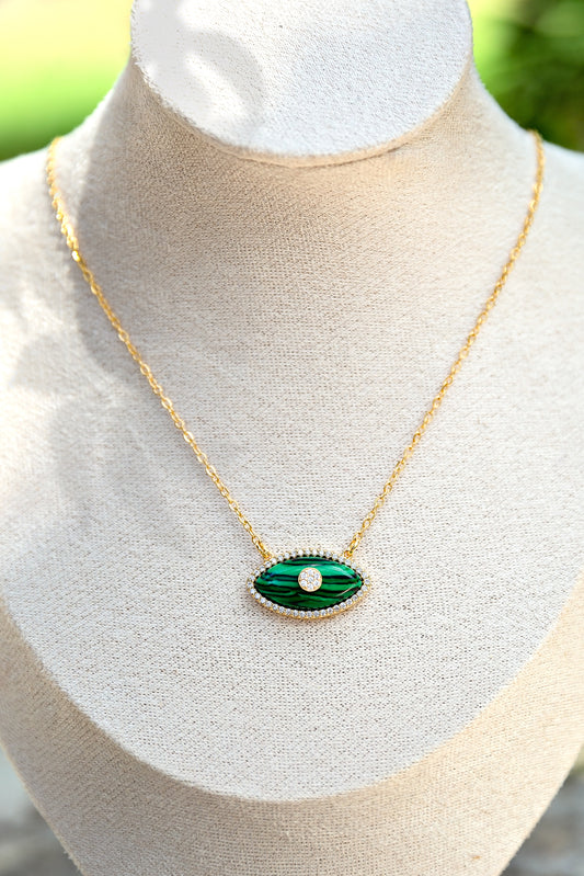 Gold necklace with a green eye-shaped pendant on a mannequin bust.