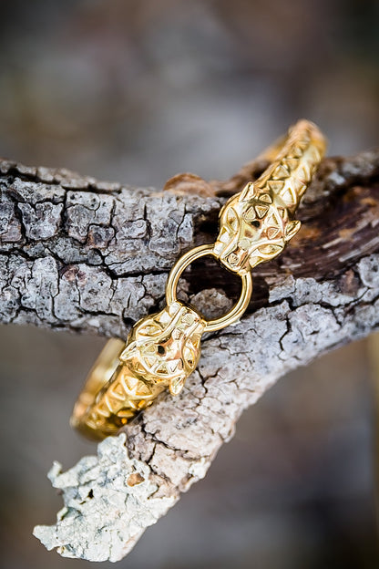 Gold feline-inspired bangle bracelet displayed on a tree branch, showing detailed textured design and circular center clasp