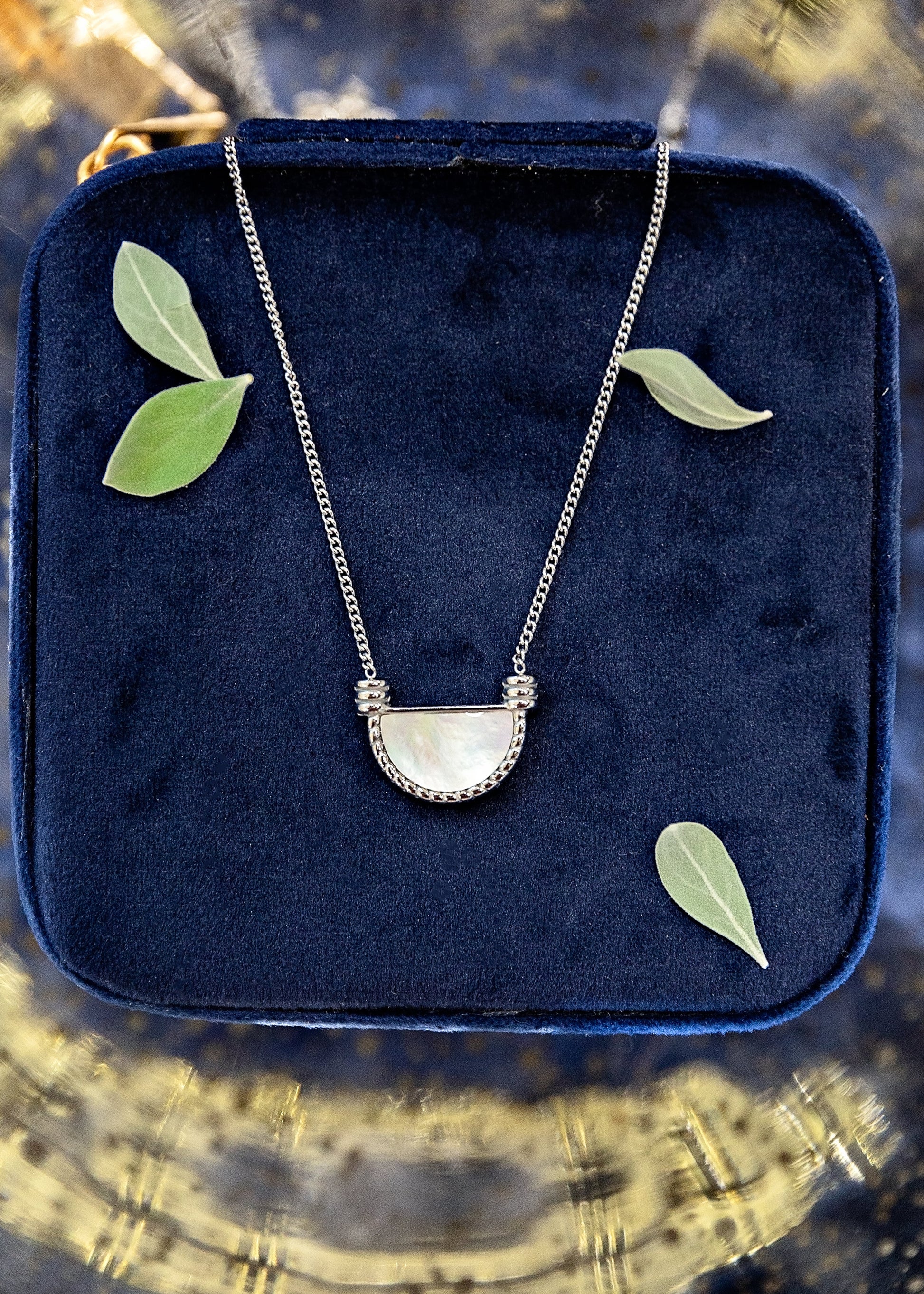 Necklace with a half-moon pendant on a blue velvet cushion with leaves