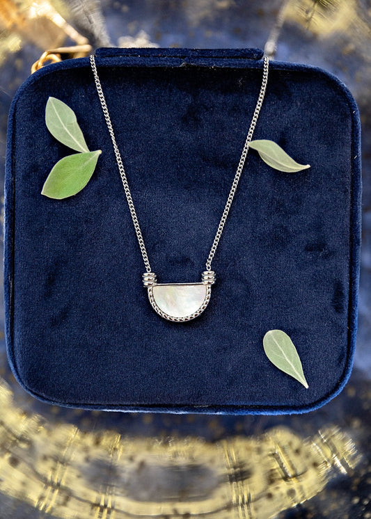 Necklace with a half-moon pendant on a blue velvet cushion with leaves