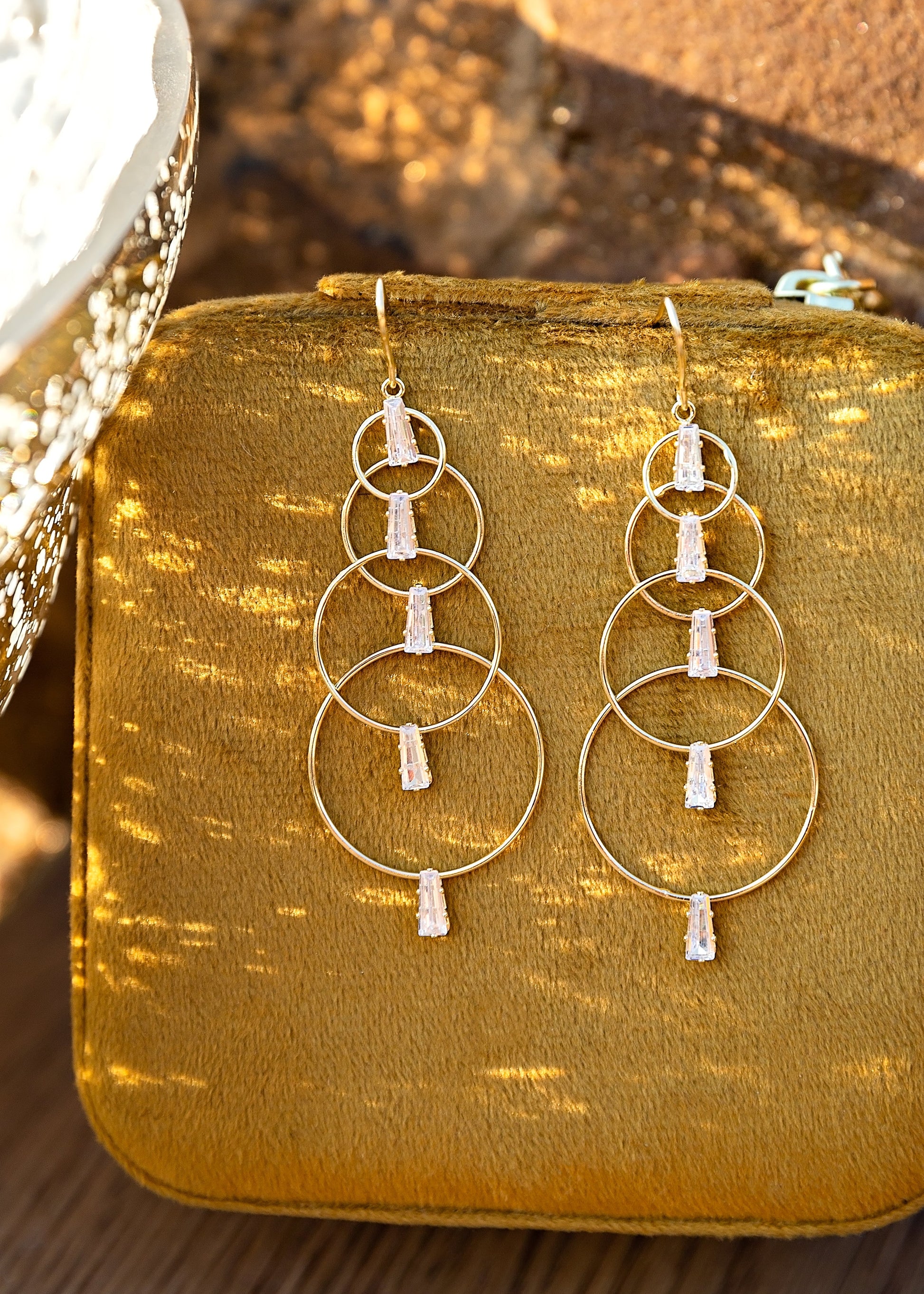 Gold hoop earrings with white stones on a mustard yellow fabric background