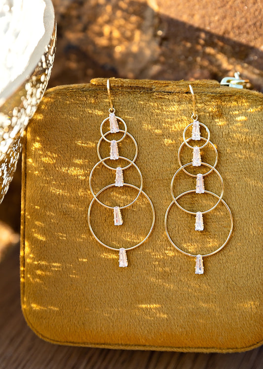 Gold hoop earrings with white stones on a mustard yellow fabric background