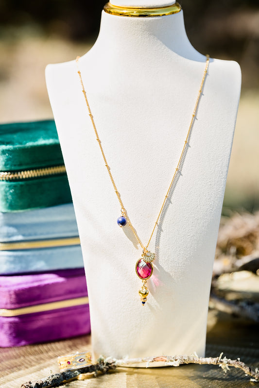 Long gold layering necklace with multiple charms including lapis stone, glass pendant, and zircon accents displayed on a jewelry bust