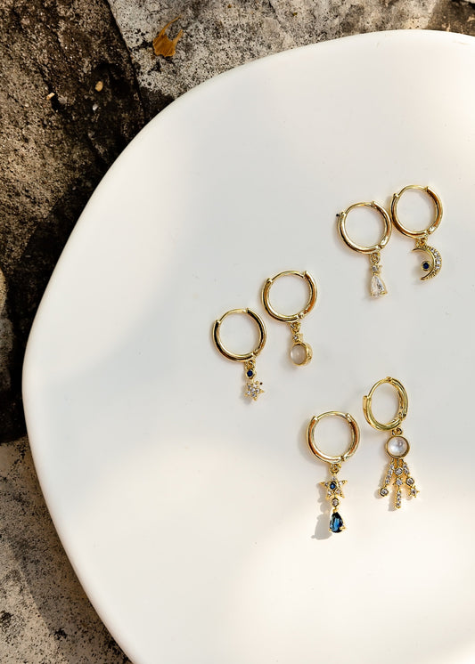 Gold earrings with small gemstones on a white plate against a stone background