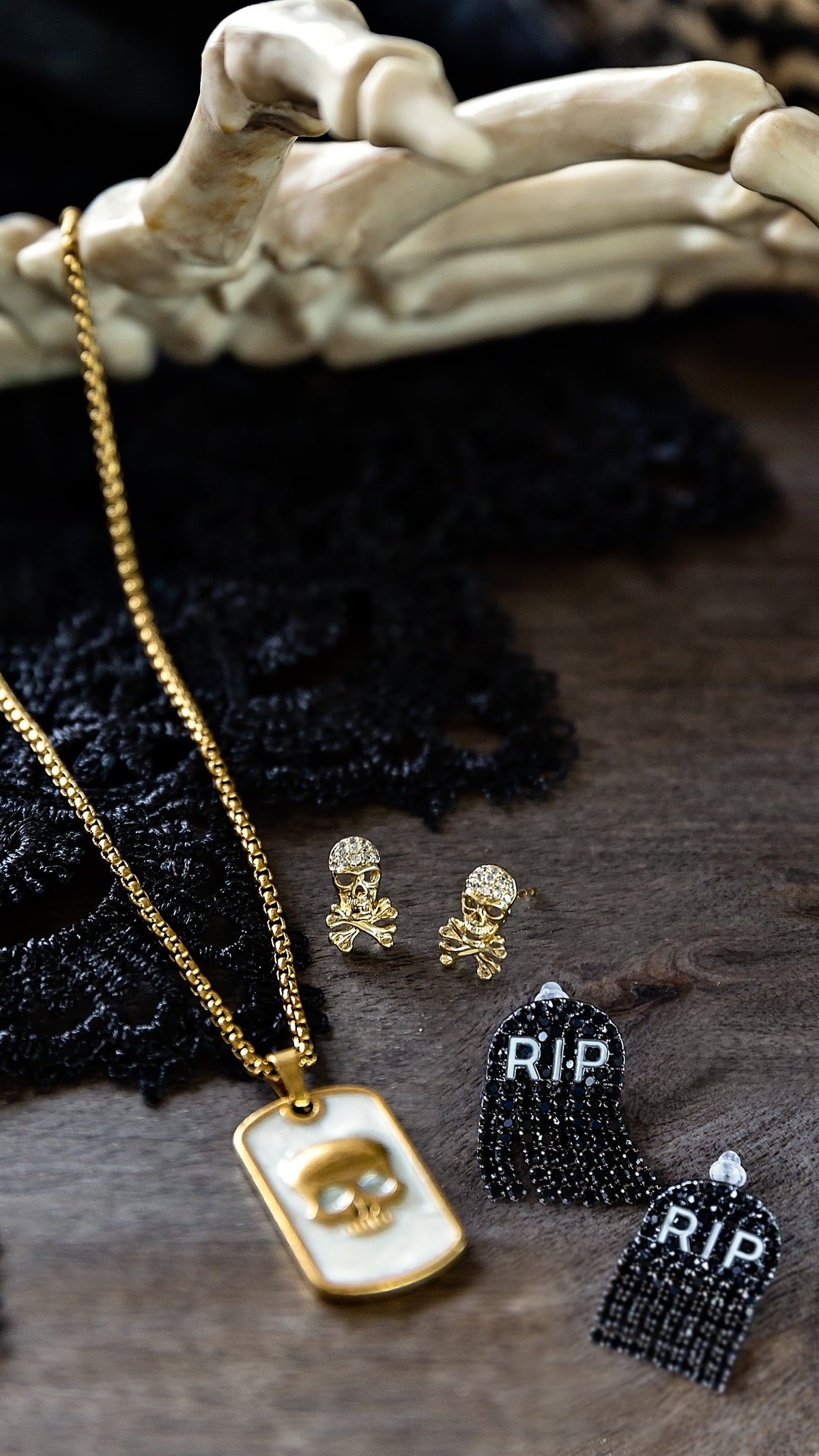 Skull Micro Stud Earrings by VEITA Jewelry styled alongside gold jewelry and dark textured accessories in a rustic setting.