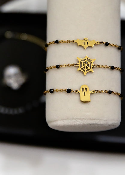 Three gold bracelets with black beads on a white cylindrical stand.