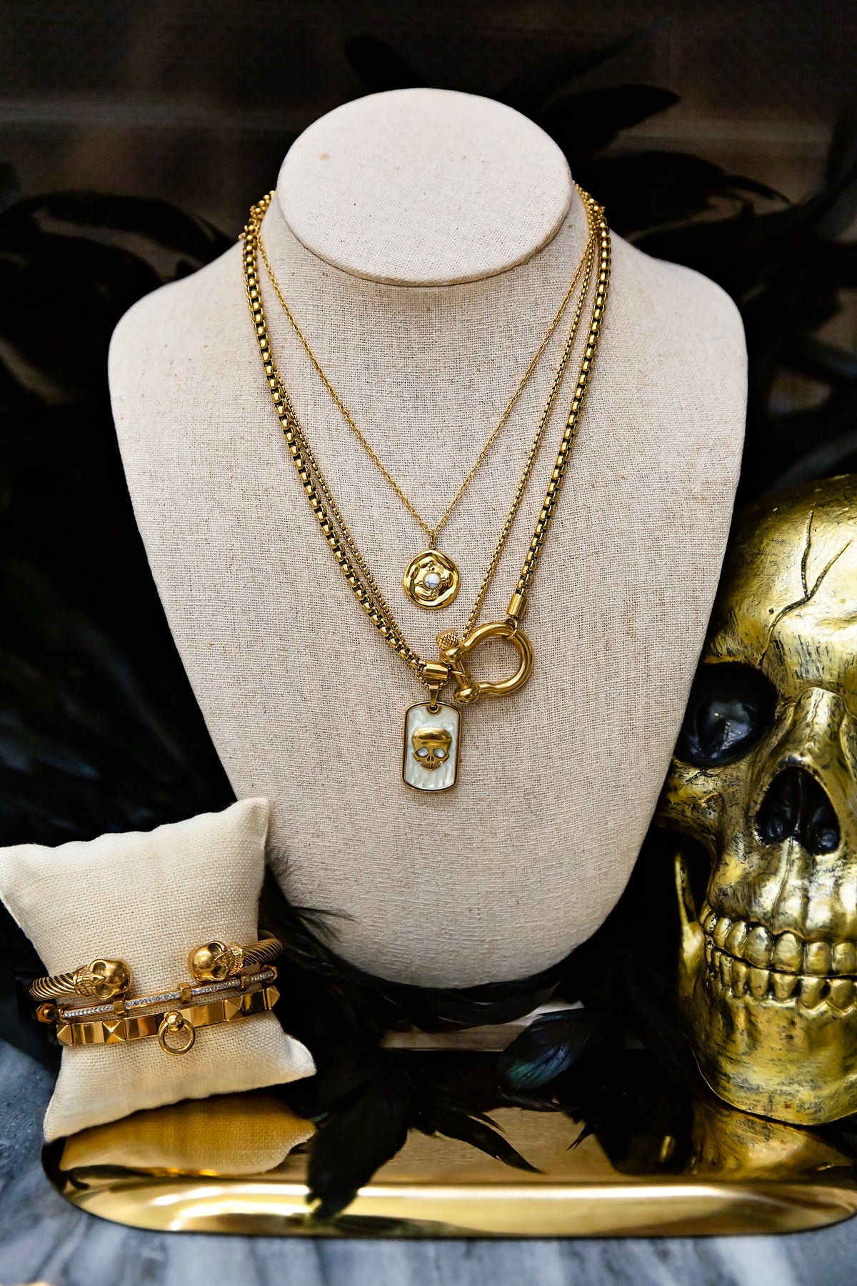 Gold necklaces on a mannequin bust with a gold skull and ring beside it.