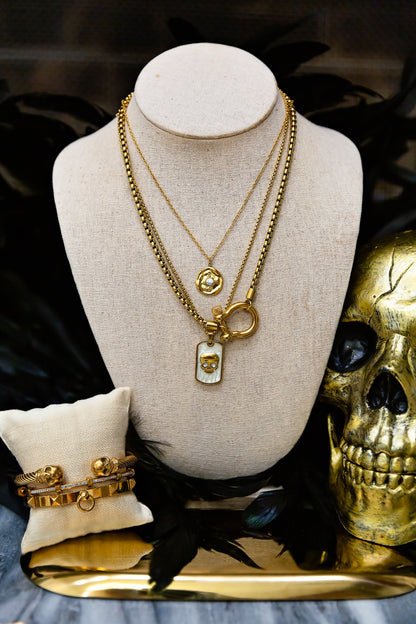 Gold necklaces on a mannequin bust with a gold skull and ring beside it.